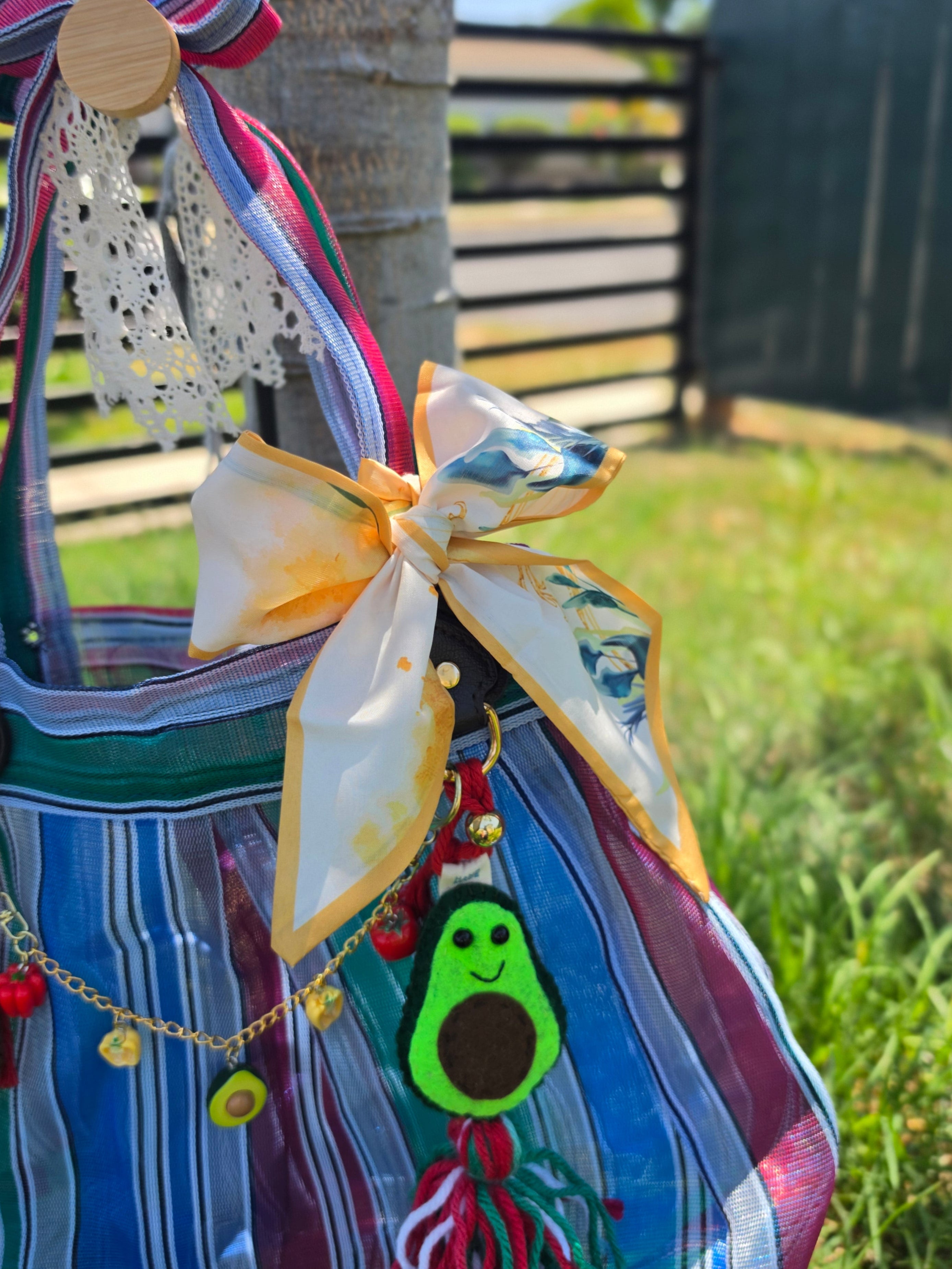 Detalle de moño floral amarillo y blanco con charm de aguacate en bolsa de mercado mexicana de rayas azul y morado