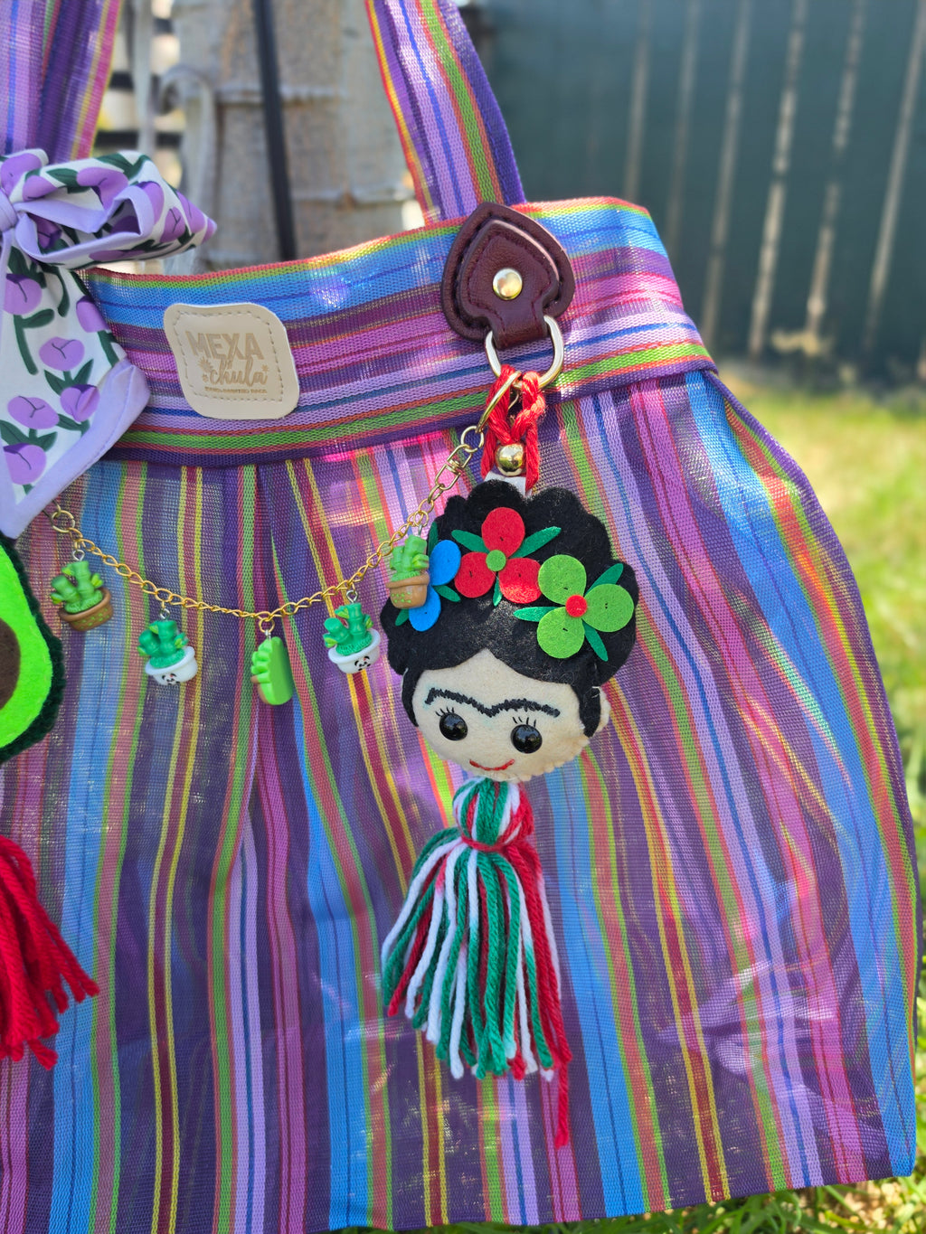 Bolsa de mercado mexicana colgada de un árbol, mostrando charms de aguacate y Frida Kahlo con borlas roja y tricolor