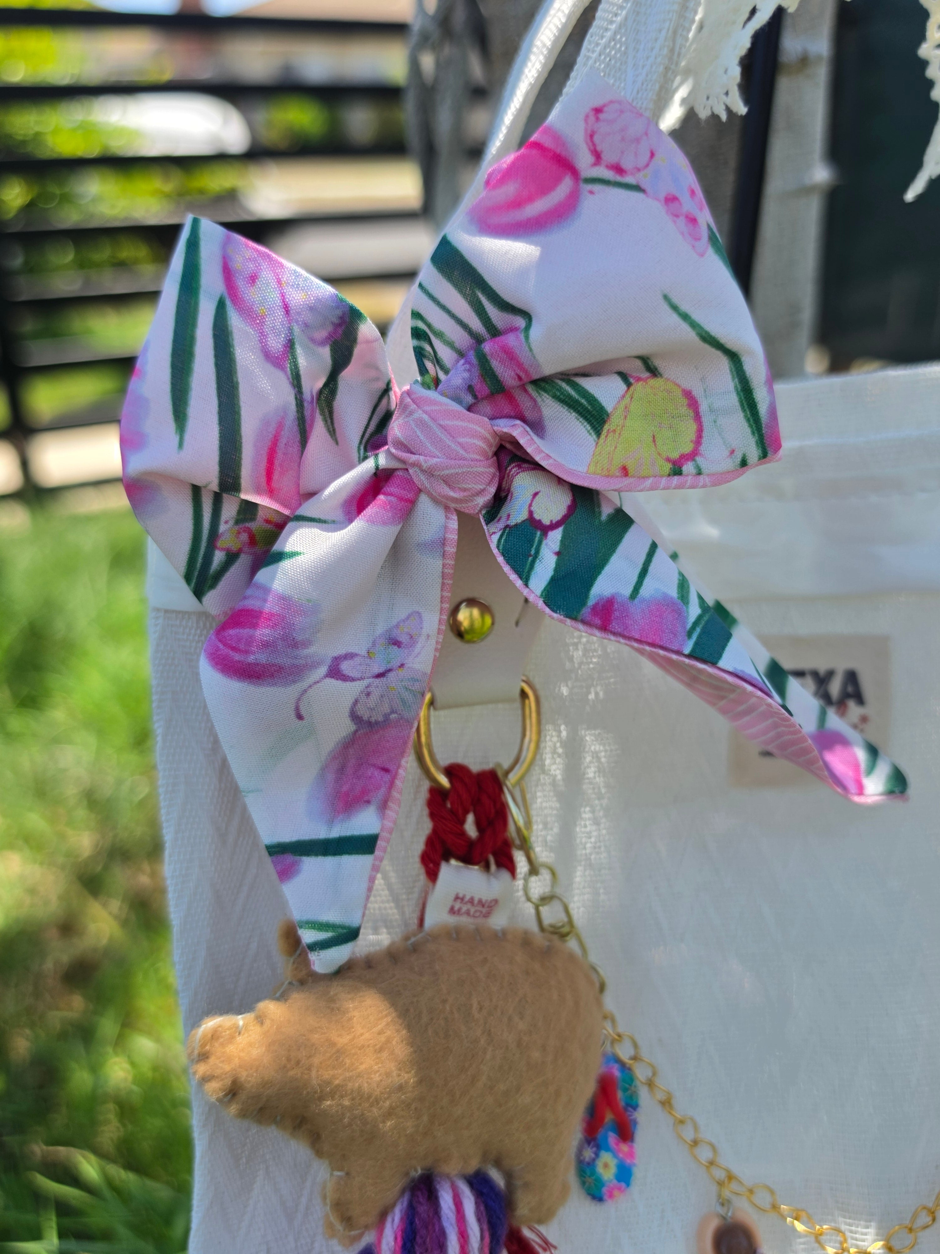 Detalle del moño floral rosa y charm de cerdita de fieltro en bolso de mercado mexicano color blanco