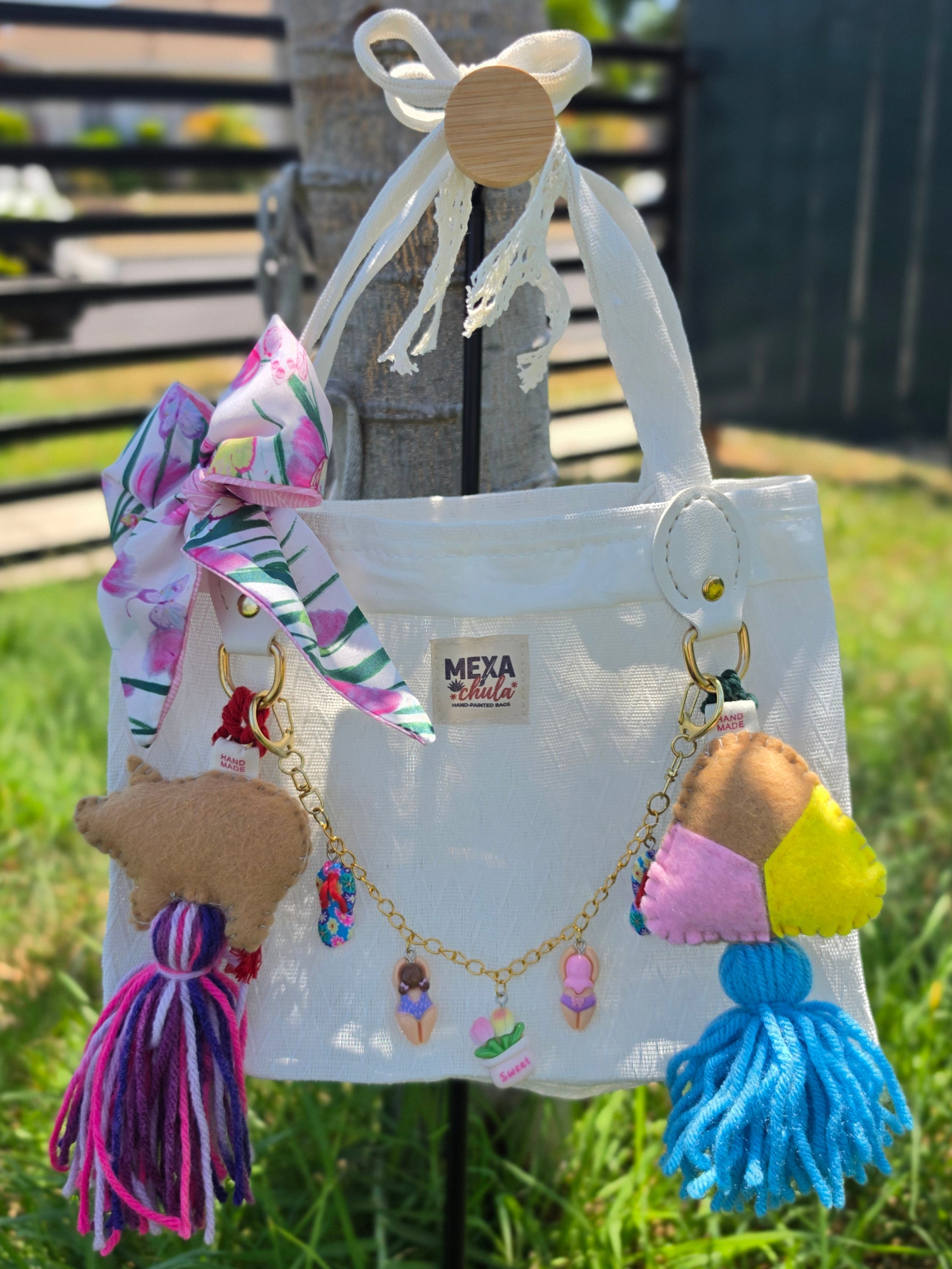 Vista frontal de bolso de mercado mexicano blanco con charms de cerdita y concha y cadena de dijes