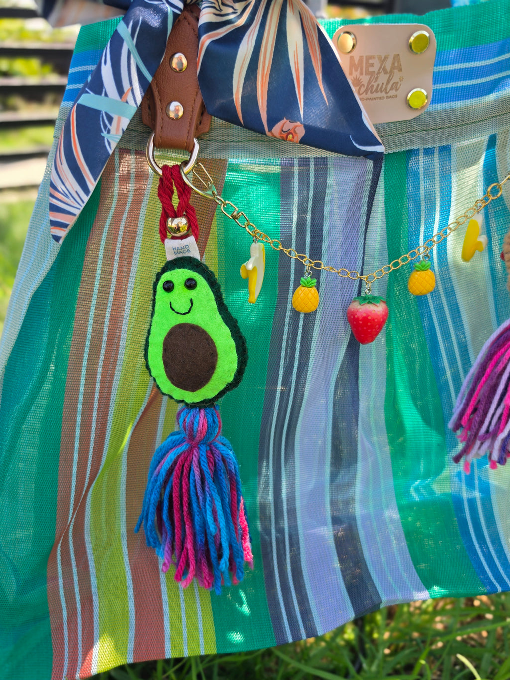 Charm de aguacate de fieltro con borla azul y rosa y cadena de charms de piña y fresa en bolsa de mercado mexicana