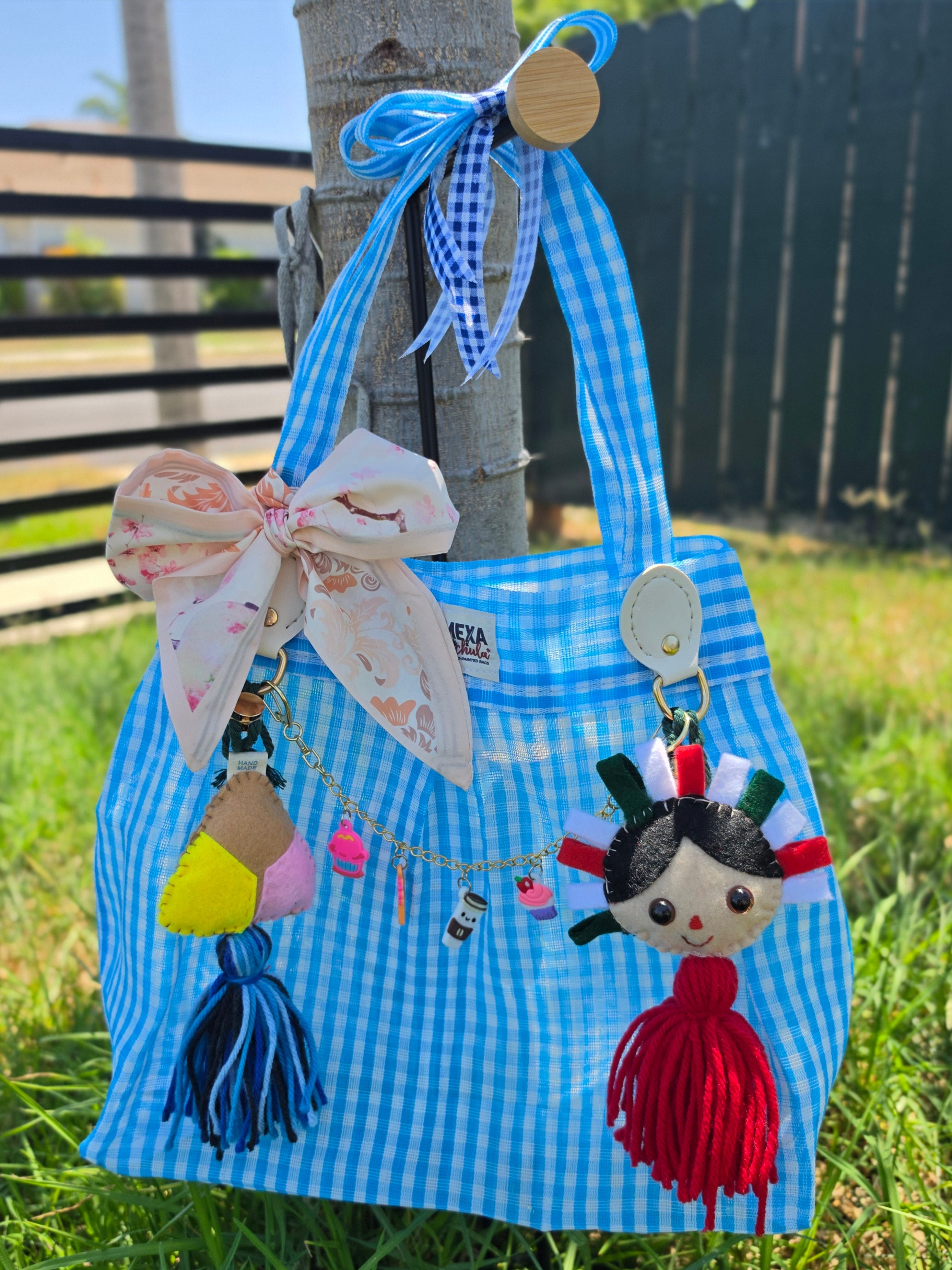Vista frontal de bolsa de mercado mexicana artesanal con moño floral y charms de concha y muñequita hechos a mano