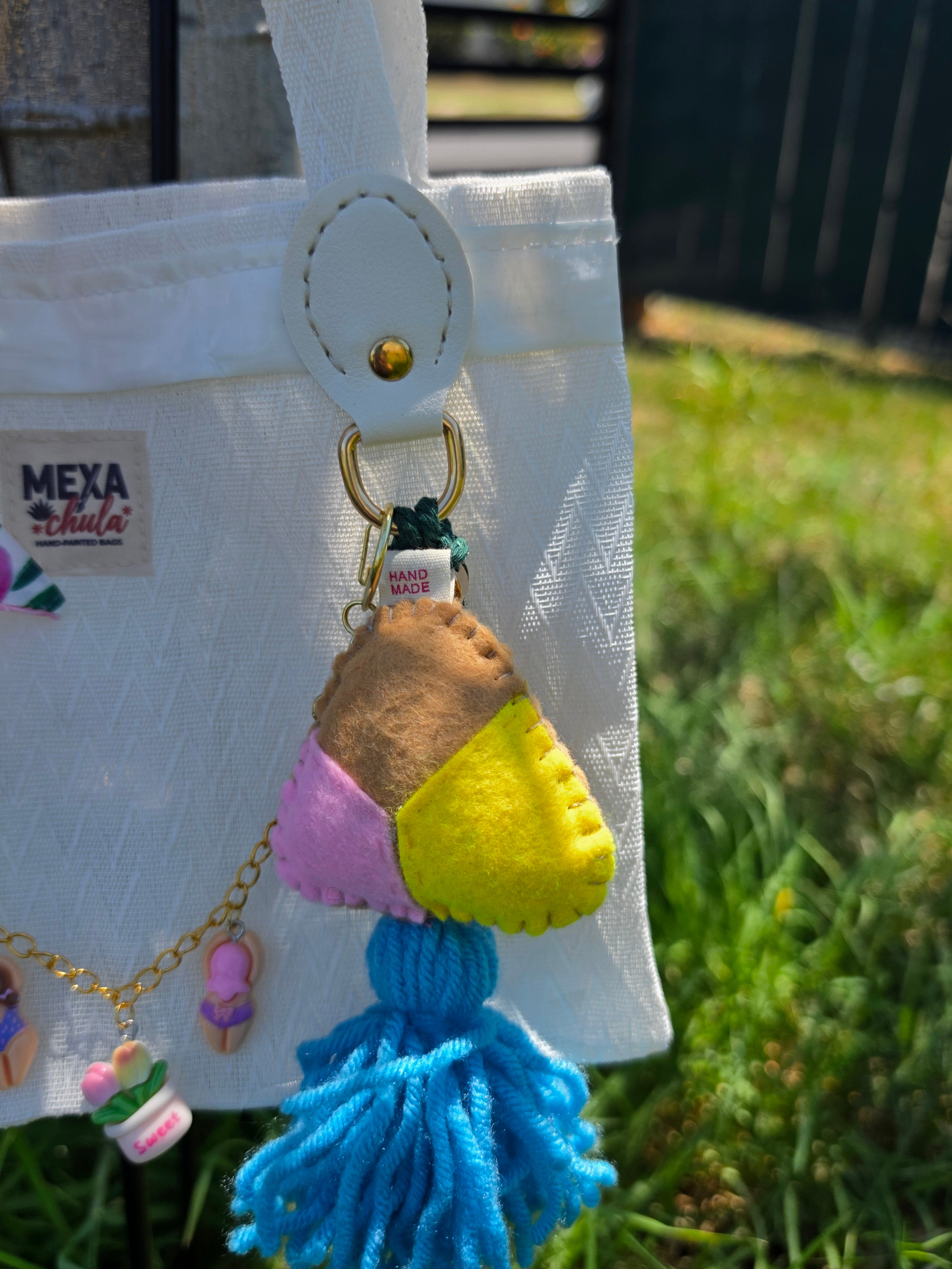 Charm de concha de fieltro en tonos rosa, amarillo y café con borla azul en bolso de mercado mexicano